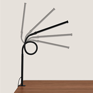 Minimalist desk lamp with adjustable arm in dark metal finish, mounted on wooden surface. Lamp demonstrates range of motion positions.