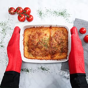 Red silicone gloves safely holding a hot baked lasagna dish.