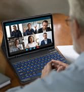 a man sitting at a desk with a laptop and a group of people on the screen