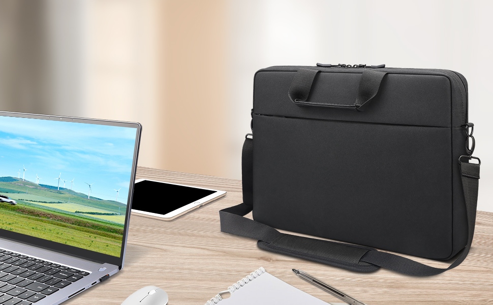 Black laptop bag or sleeve with handle and strap, displayed next to an open laptop on a wooden desk with office supplies.