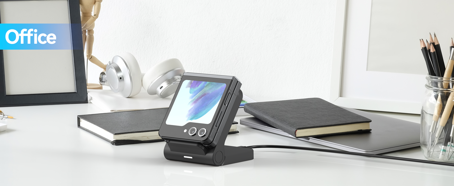 Small portable device with holographic display on desk. Square shape with buttons, stand for angled viewing. Surrounded by office supplies like notebooks and pencils.