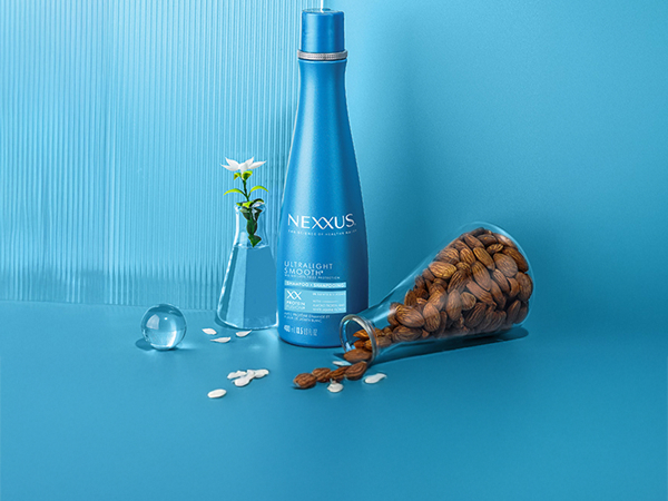 Nexxus bottle between a flower in a vase with water and a spilled lab glass filled with ingredients.