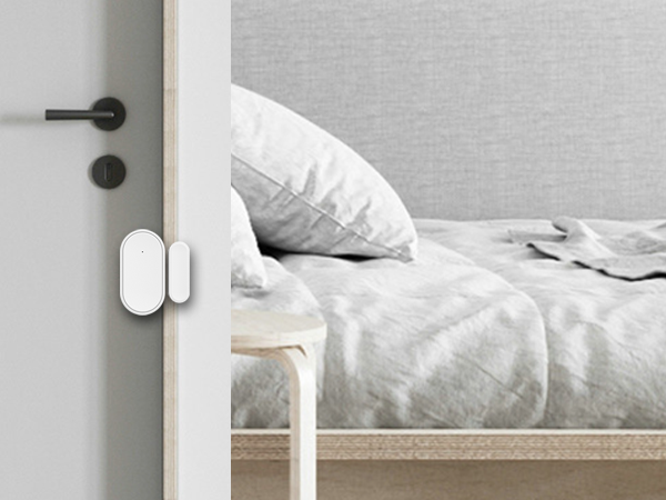 Minimalist bedroom interior with white bedding and wall-mounted door sensor or security device in white.