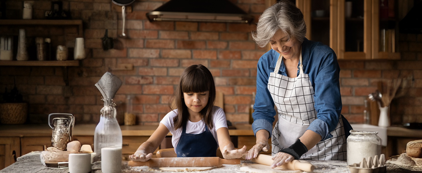 Kitchen scene with wooden table covered in flour and dough. Baking ingredients and tools visible, including eggs, milk bottle, and rolling pin.