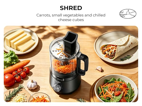 Mini food processor shredding carrots beside cheese, a salad and a filled wrap. 