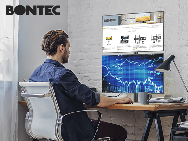 Bontec dual monitor setup on wooden desk showing financial charts and graphs. White mesh office chair and industrial-style workspace environment.