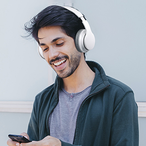 Person wearing white over-ear headphones, smiling while looking at a smartphone.
