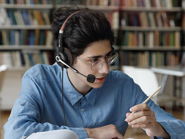 A boy wearing ARA700 wired headset is taking an online class in the library.