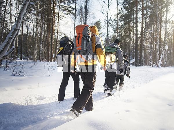 Group of hikers walking through snowy forest trail. People wearing winter gear and carrying large backpacks for outdoor winter activities.
