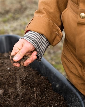 a hand picking up soil and sprinkling it in bin