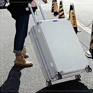 Large white hardshell suitcase with ribbed exterior and wheels. Person pulling luggage on street, demonstrating its use for travel.