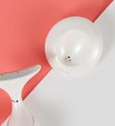 Close-up partial view of a white spherical light fixture or lamp component against a coral-colored background.
