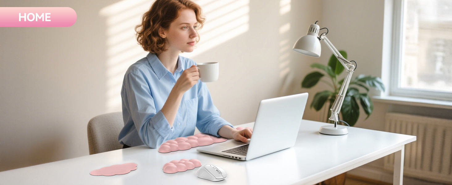 Person working at white desk with laptop, desk lamp, and plant. Holding coffee mug while typing. Decorative pink and gray shapes on desk surface.