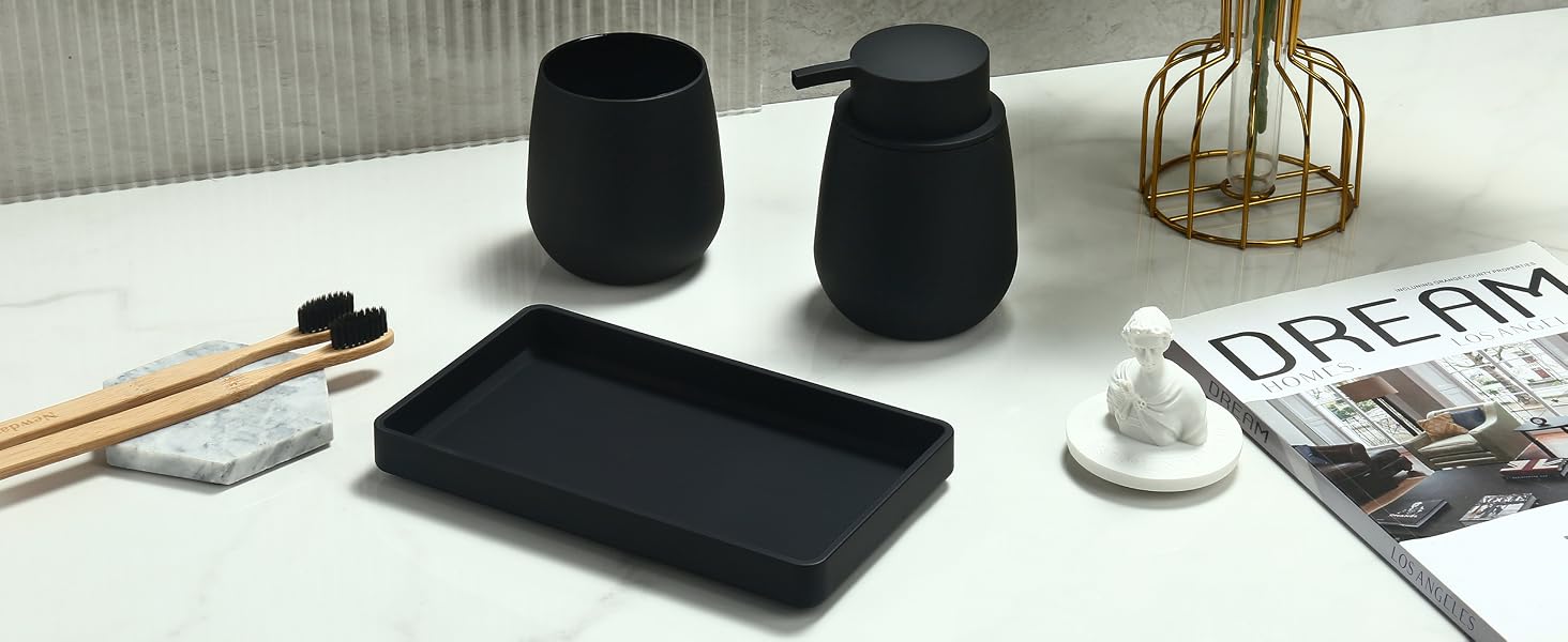 Bathroom accessories set on white surface: two black ceramic containers, wooden toothbrushes, black rectangular tray, small white ceramic figurine, and partial view of a magazine.