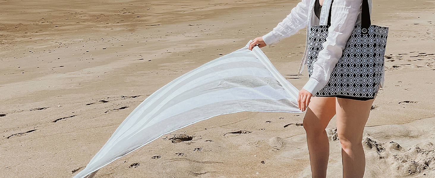 A beach towel waving in the air as a woman moves to place it down on the sandy beach