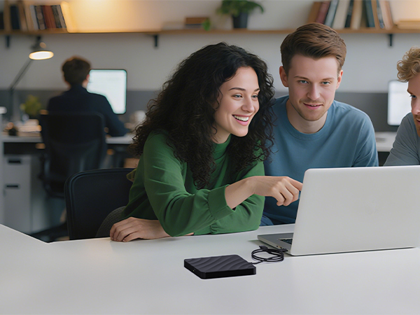 People working collaboratively at a desk with laptop in modern office setting with natural lighting.