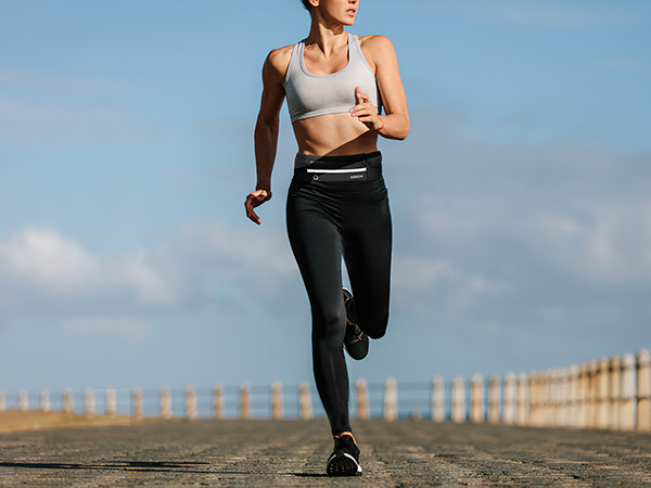 Athletic person jogging on a paved path against blue sky, wearing black leggings and light-colored athletic top.
