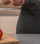 Partial view of a kitchen counter with a wooden cutting board and a red tomato. A hand is visible in the upper left corner.