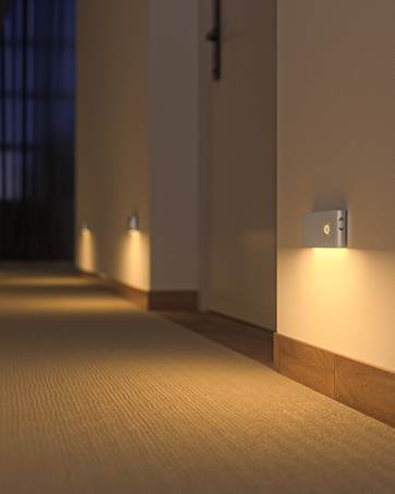 Motion-sensor wall light creating warm ambient lighting in a hallway, illuminating carpeted floor and white walls with soft golden glow.