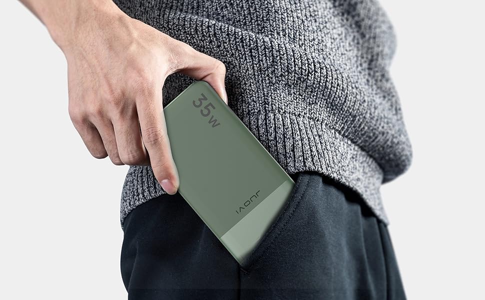 Hand holding a green, rectangular portable device, possibly a power bank or mobile charger. Person wearing gray sweater.