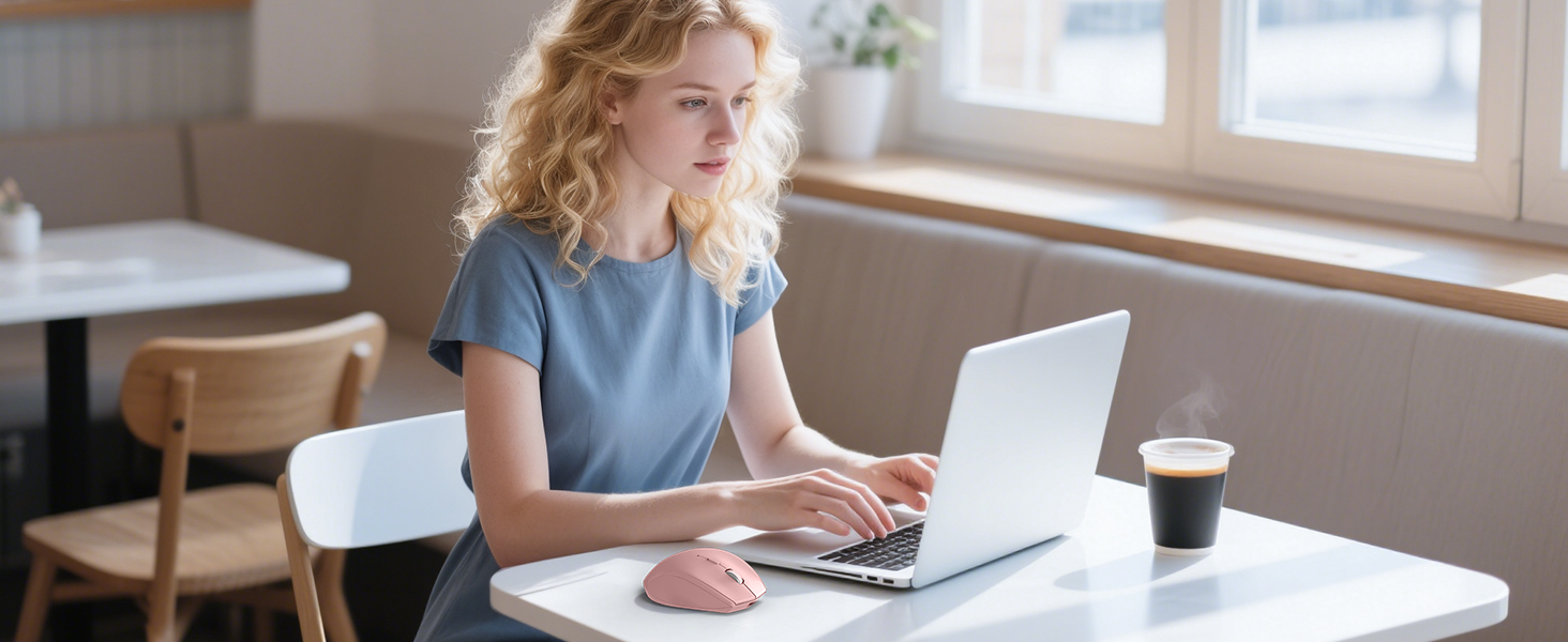 Person seated at white desk in sunlit room working on laptop computer with coffee cup nearby.