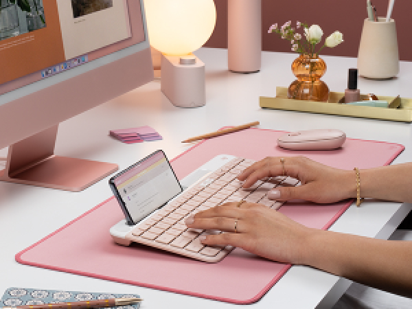 a woman typing on k585 slim compact wireless rose keyboard with phone holder