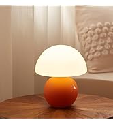 Modern mushroom-shaped table lamp with orange ceramic base and white frosted glass dome shade, placed on wooden surface with sunlit background.