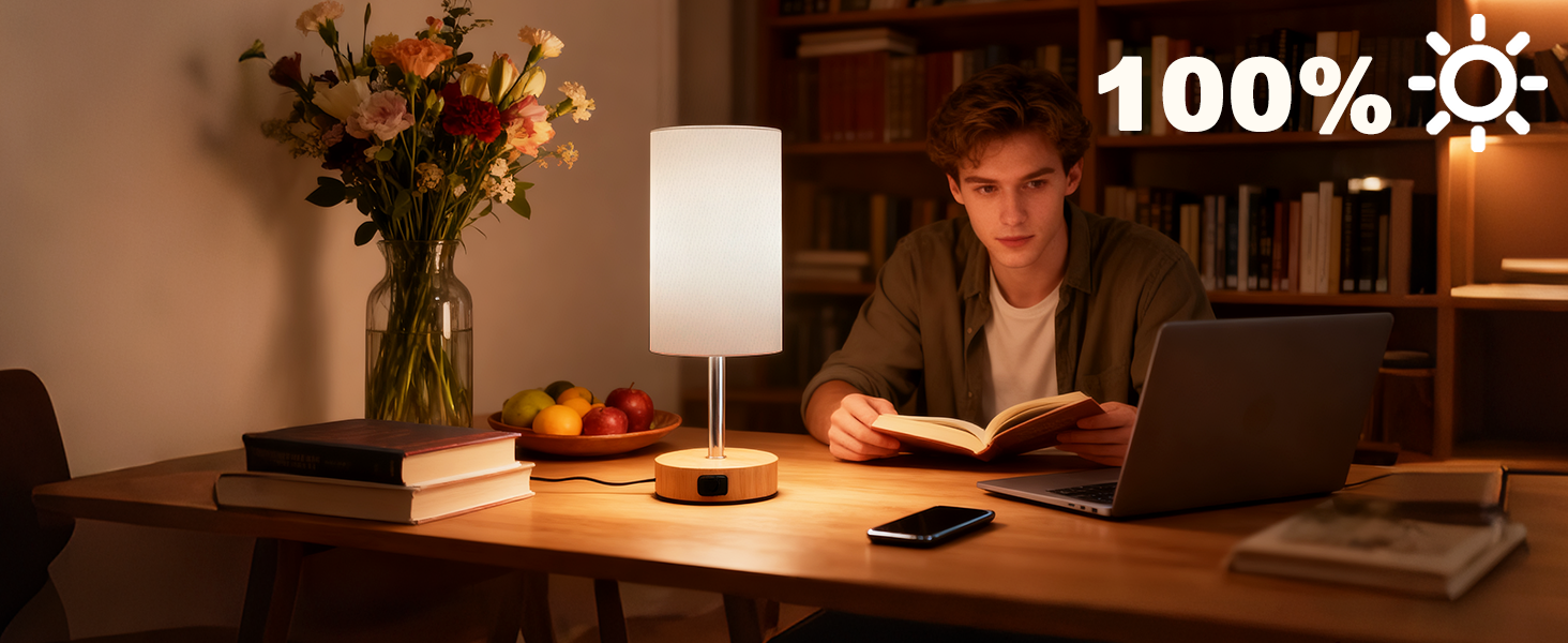 Text reads '100%'. Desktop workspace setup with desk lamp providing warm lighting, showing laptop and study/work materials in evening/night setting.