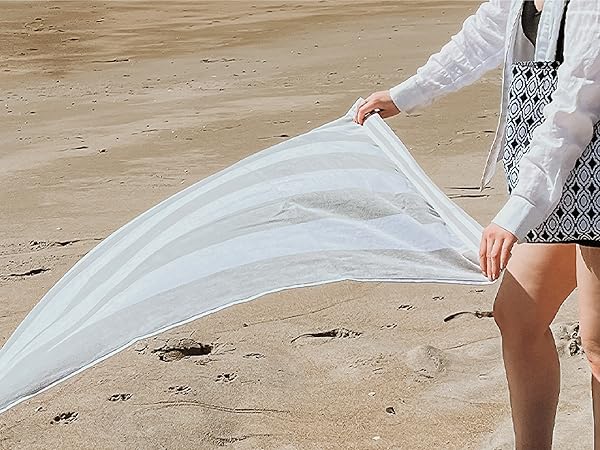 A beach towel waving in the air as a woman moves to place it down on the sandy beach