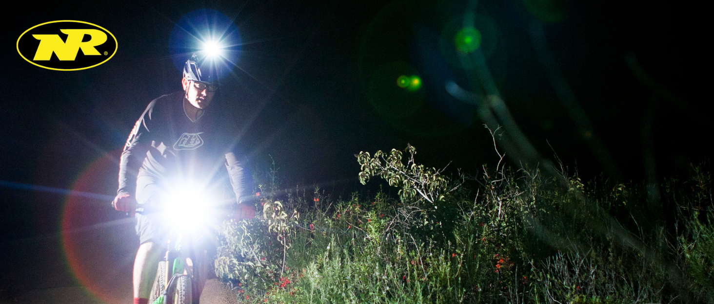 Mountain biker night riding with bright front and helmet lights surrounded by brush and wildflowers
