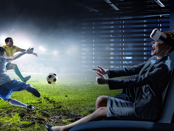 Virtual reality headset user experiencing immersive soccer game, with player kicking ball in simulated stadium environment.