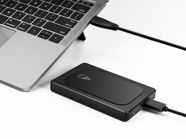 External hard drive connected to laptop. Black, rectangular device with USB cable plugged into silver laptop, showcasing portable data storage solution.
