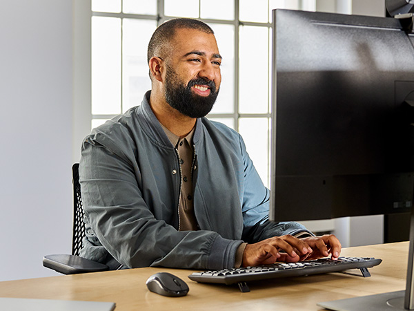 a man working on a computer using mk370 combo for business wireless keyboard and mouse
