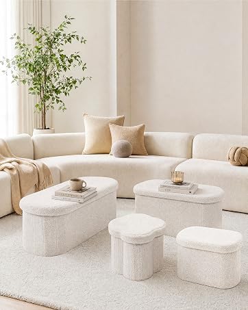 Minimalist living room interior with cream-colored curved modular sofa, natural wood plant stand with greenery, and three cream upholstered pouf ottomans on light area rug.