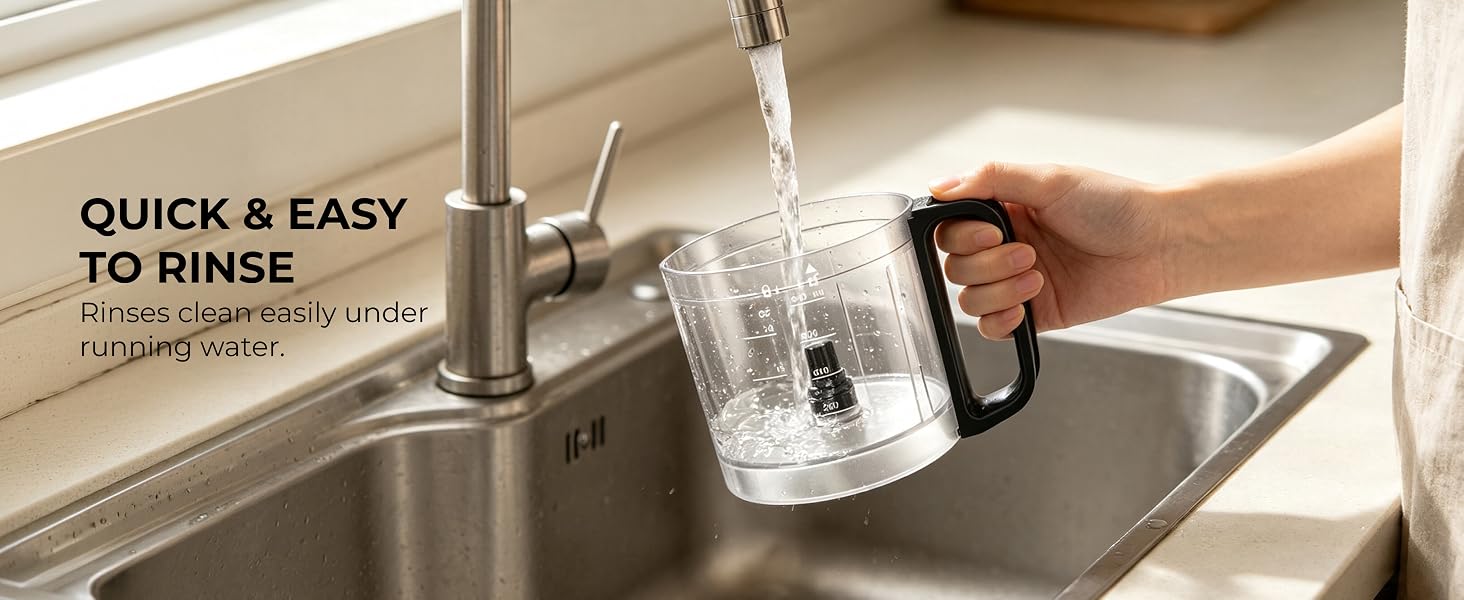 Hand rinsing the removable 4-cup processor bowl under running water in a kitchen sink.