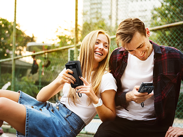 a couple of young people are sitting on the ground and using their phones.
