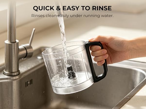 Hand rinsing the removable 4-cup processor bowl under running water in a kitchen sink.