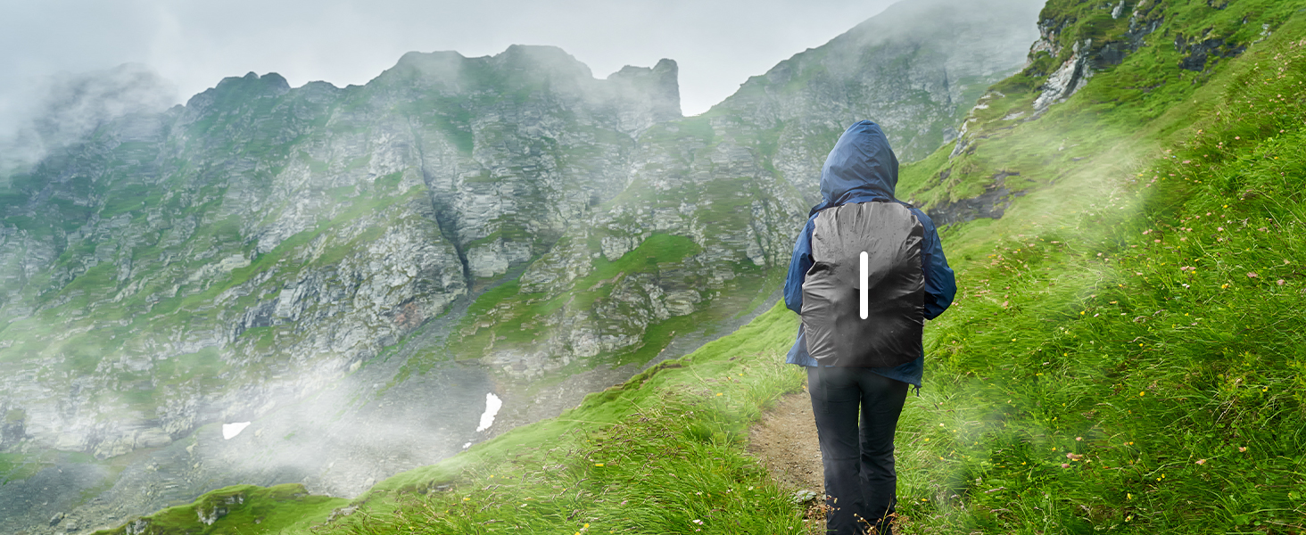 Hiker in dark jacket on misty green mountainside. Fog-covered peaks visible in background.