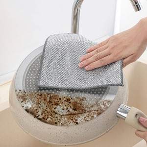 A hand cleaning a grey textured surface over a bowl containing grain or seeds. Water is flowing from a faucet into the bowl.