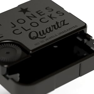 Close-up of a black Jones Clocks Quartz movement. The mechanism is partially visible, with 'NO JEWELS UNADJUSTED' engraved on the metal surface.