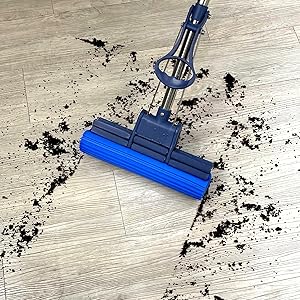 Blue and silver mop cleaning scattered dirt on a light-colored wooden floor.