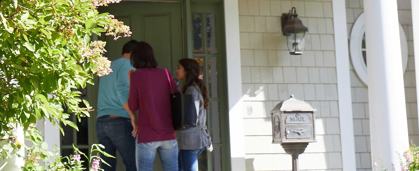 Family entering front door of home, push button doorbell installed to side of door