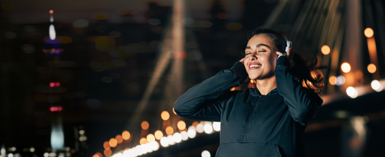 a woman in a black jacket smiles at the camera while standing in the street at night.