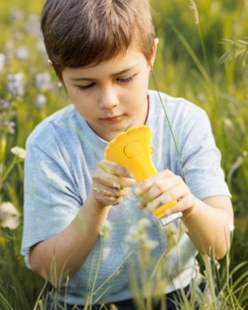 Yellow handheld toy or device being examined in an outdoor setting with tall grass and wildflowers.