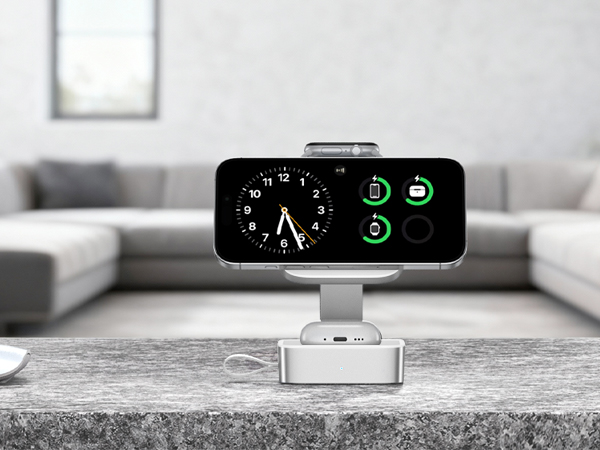 Black digital device with dual clock faces and green indicator lights mounted on white stand, photographed in living room setting with blurred furniture background.