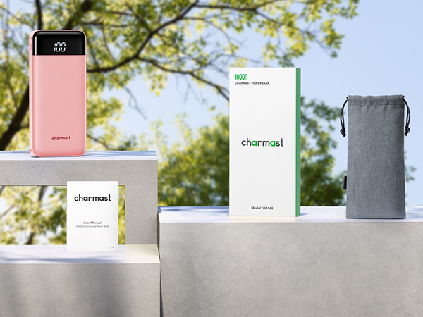 Pink power bank, white box, and gray pouch displayed on concrete steps outdoors. 'Charmast' brand visible on products.