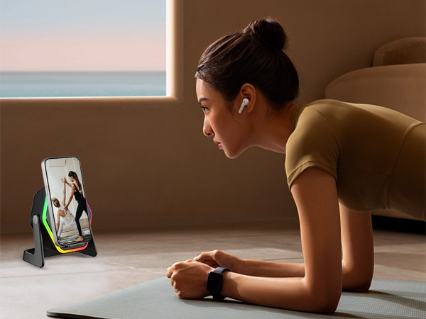 Person exercising in plank position on mat, viewing tablet device propped on stand during home workout session at sunset.