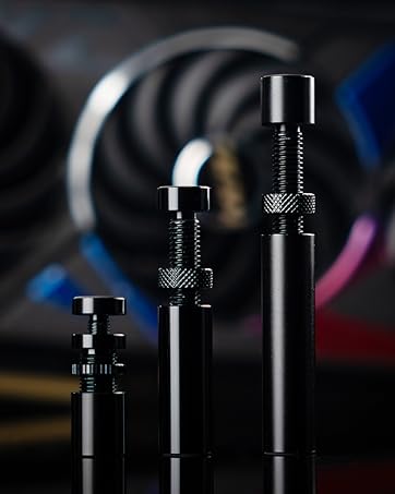 Three black metal cylinders of increasing height with textured grips and smooth tops, displayed against a dark background with blurred colorful elements.