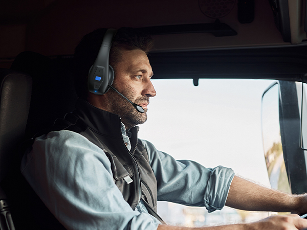 A male truck driver was driving down the road wearing a JBT100 Bluetooth headset.