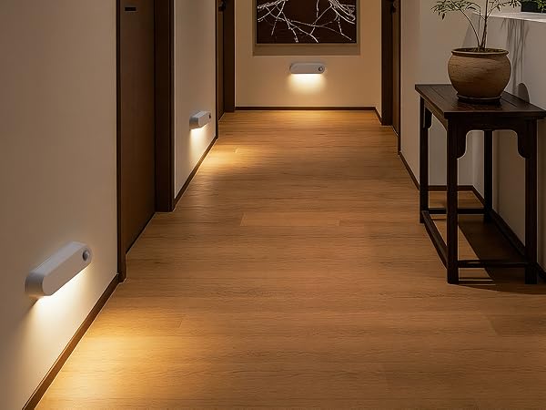 Hallway interior with illuminated wall-mounted LED lights creating ambient lighting effect along corridor. Wood flooring and decorative table visible.